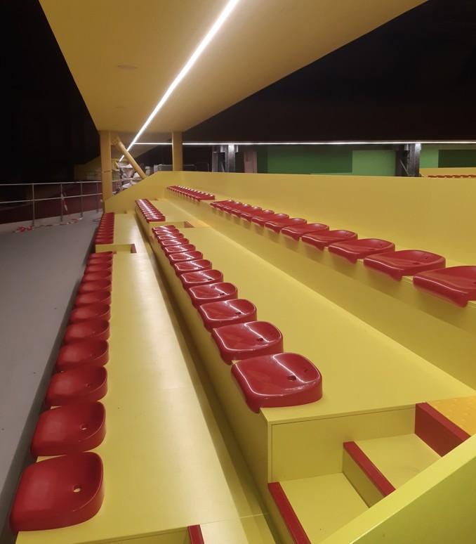 Motorisierte Teleskoptribüne mit roten Sitzschalen in einer Sporthalle mit gelben Wänden